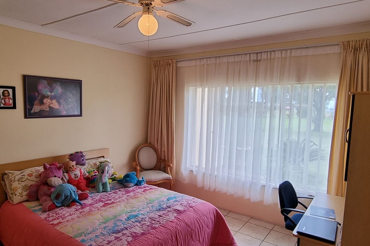 A functional bedroom featuring tiled flooring, a ceiling fan, and large windows with curtain rails, offering a comfortable and well-lit living space.