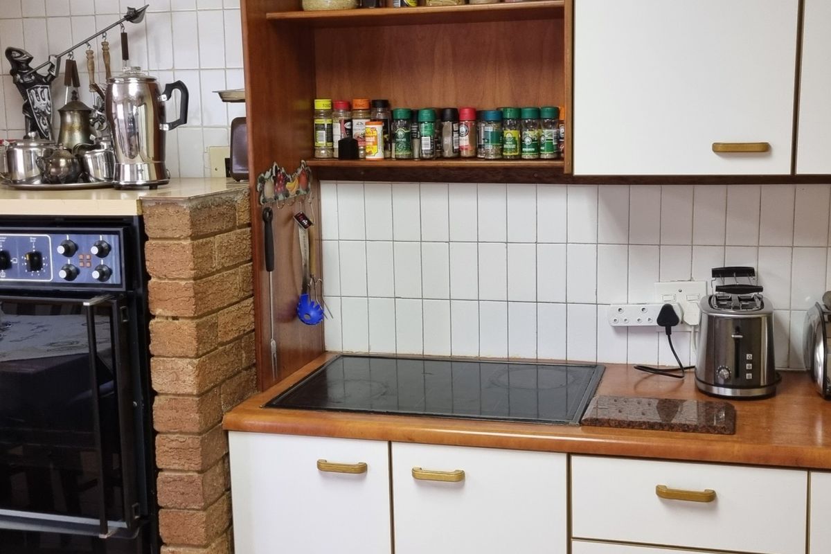 A functional kitchen area featuring a built-in oven, electric hob, tiled backsplash, and laminate countertops with integrated cabinetry.