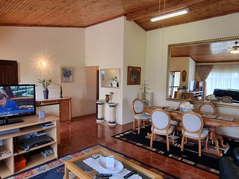 Spacious open-plan living and dining area featuring a vaulted timber ceiling, tiled flooring, and a large decorative wall mirror.