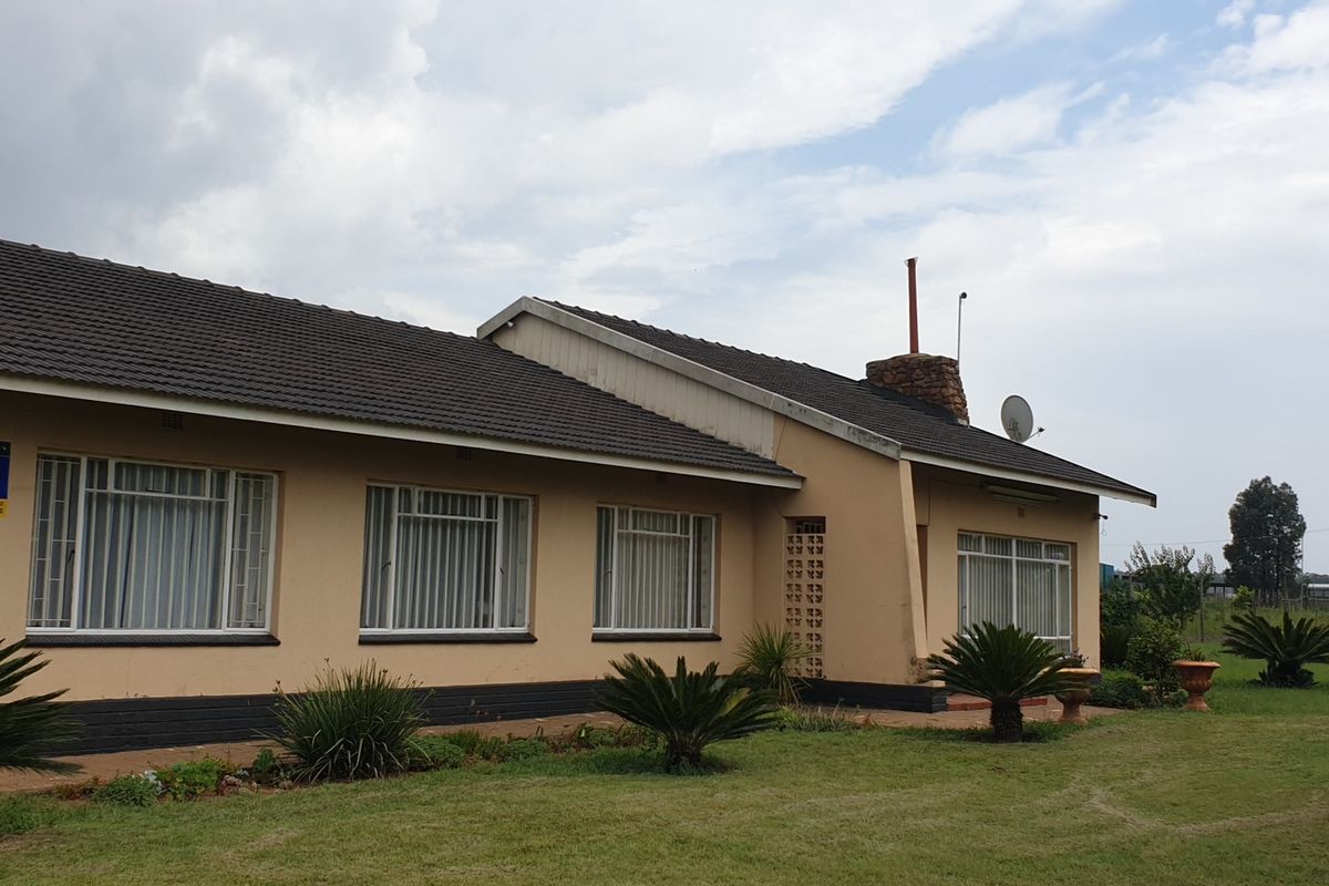 Rear view of a single-story small holding residence featuring a tiled roof, stone chimney, and established garden surroundings.