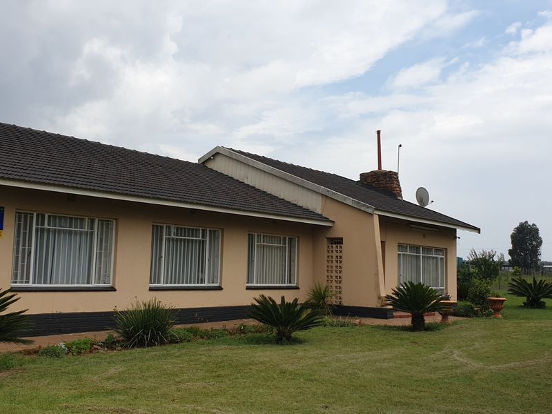 Rear view of a single-story small holding residence featuring a tiled roof, stone chimney, and established garden surroundings.