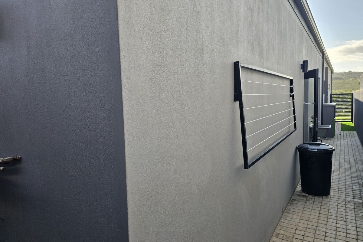 A side exterior walkway featuring a paved path, a wall-mounted clothesline, and modern grey exterior wall finishes.