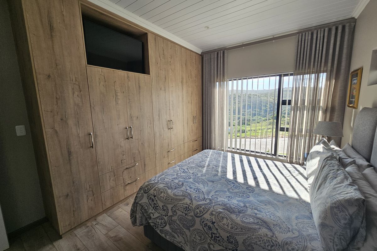 A well-maintained bedroom featuring extensive built-in timber-look cabinetry, wood-effect flooring, and a tongue and groove ceiling with scenic views.