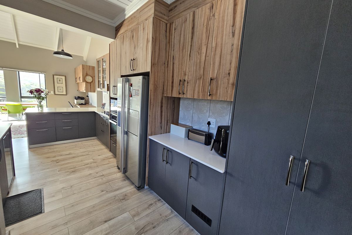 Modern kitchen featuring two-tone cabinetry, stone countertops, integrated appliances, and high vaulted ceilings with wood-look laminate flooring.