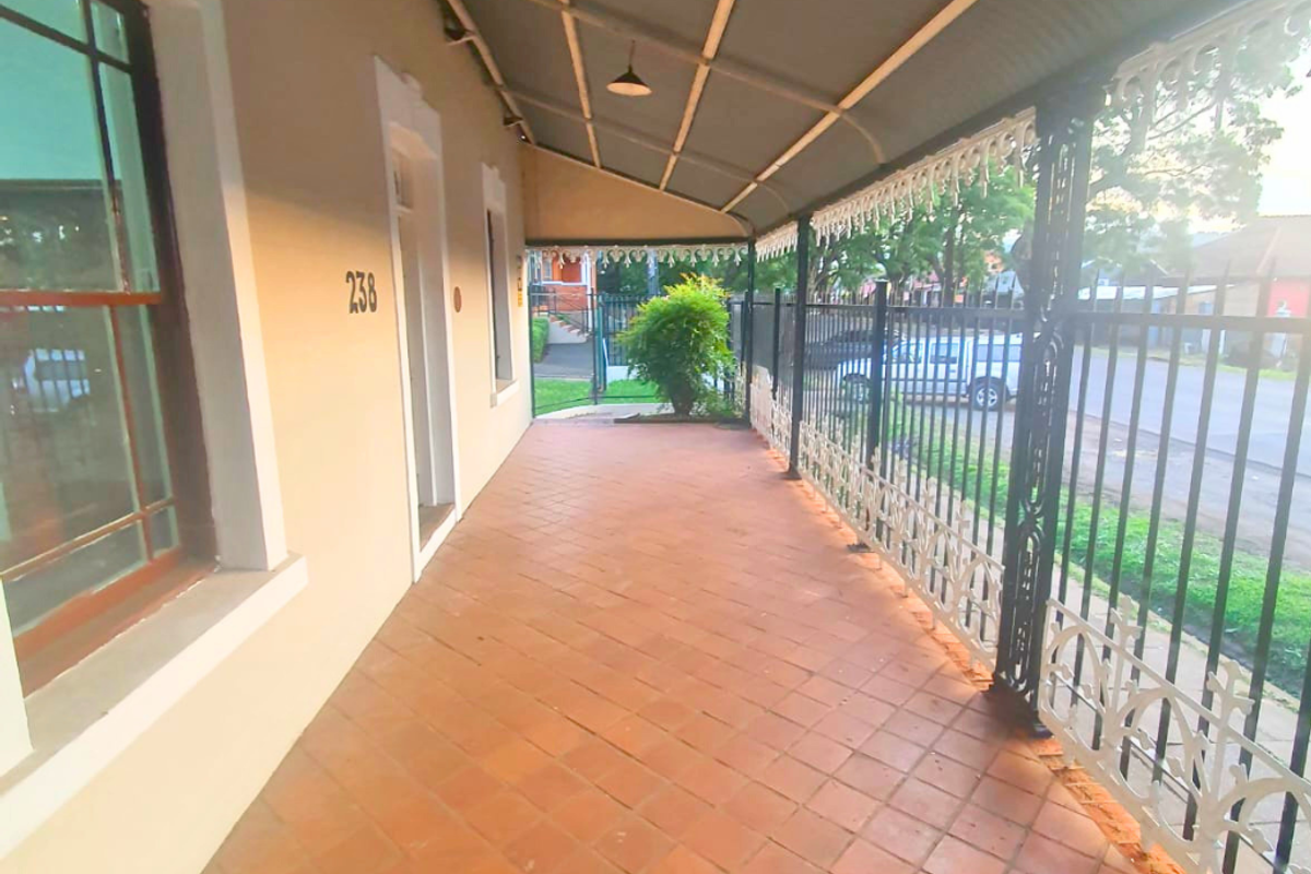 A covered front veranda featuring terracotta tiling, decorative wrought iron balustrades, and a corrugated metal roof, providing a classic street-facing entrance area.