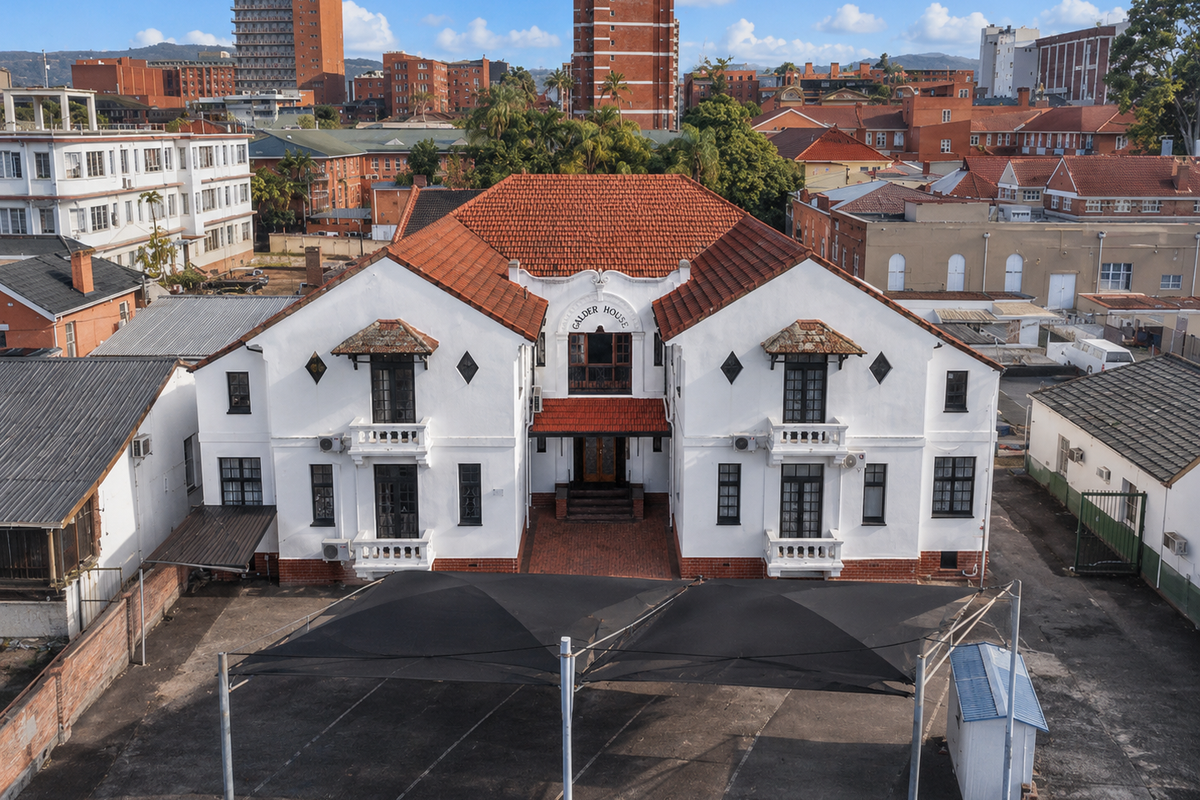 Aerial view of Galder House, a historic commercial building featuring a terracotta tile roof, balconies, and a paved parking area with shade sails.