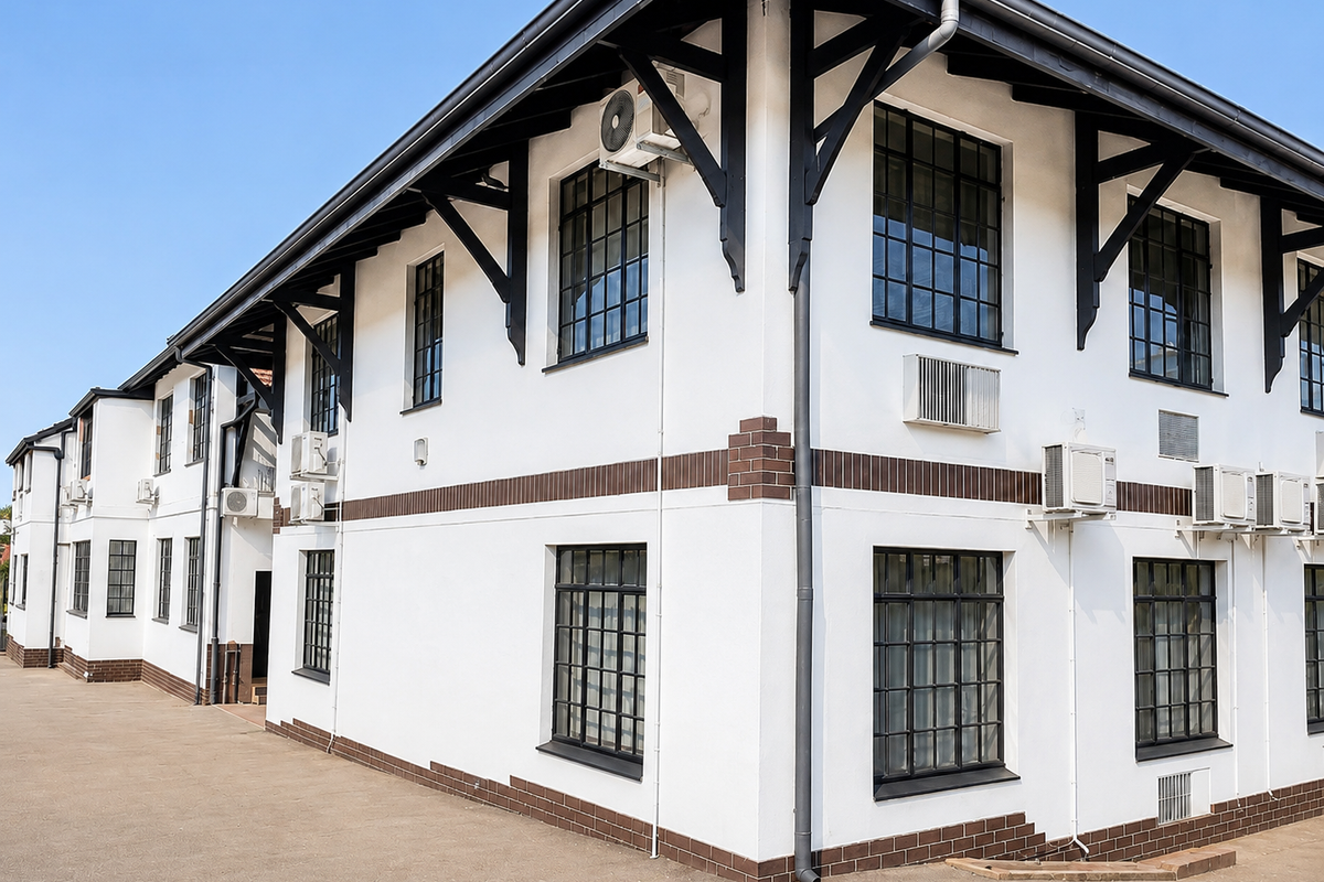A well-maintained commercial building exterior featuring white rendered walls, dark timber roof brackets, and industrial-style steel-framed windows with multiple external air conditioning units.
