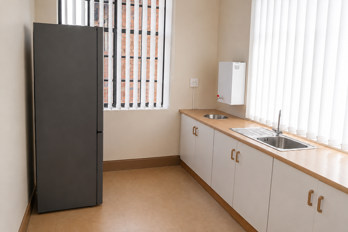 A clean, functional kitchenette featuring white cabinetry, a stainless steel sink, countertop, and wall-mounted water heater, complemented by vertical blinds.