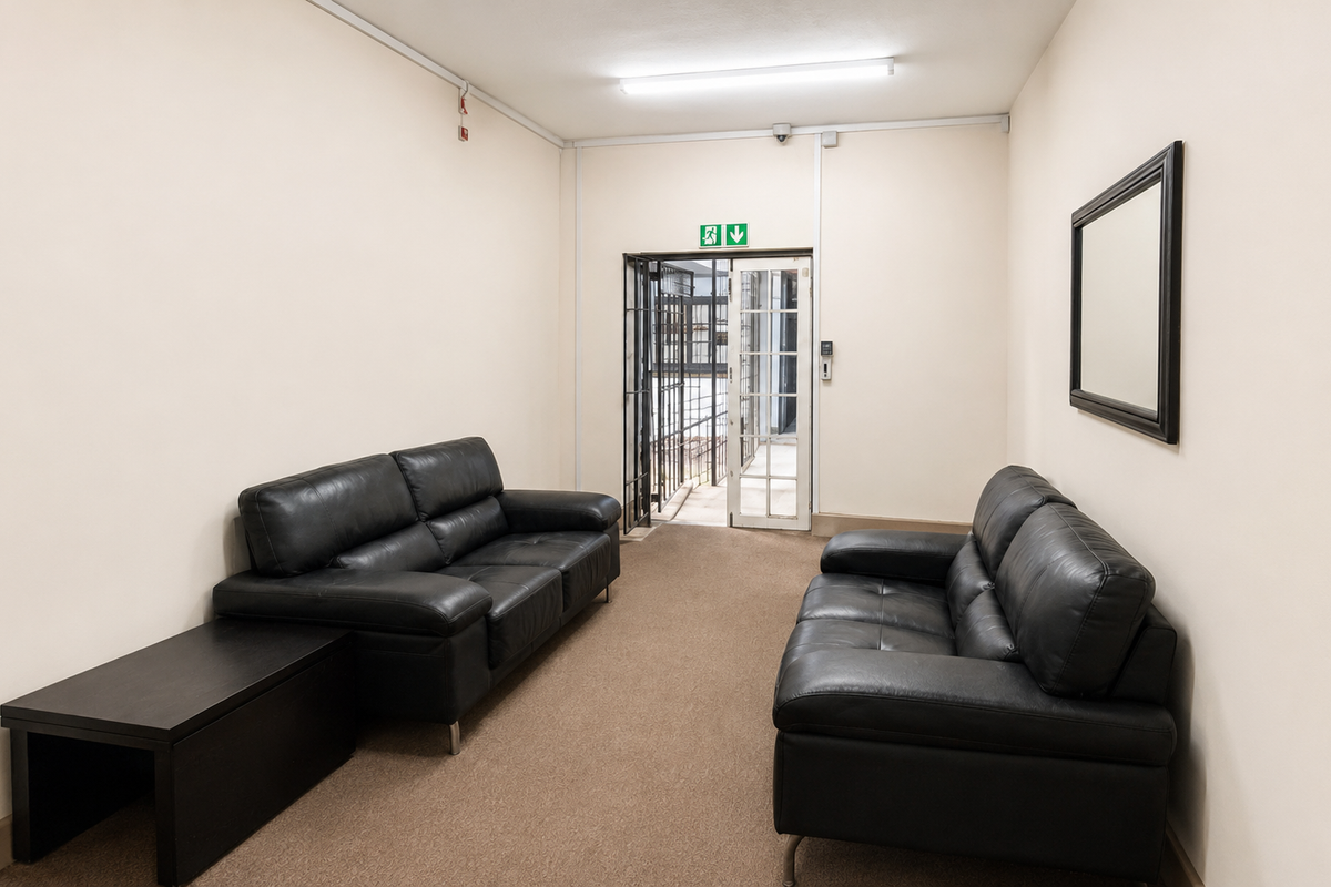 A functional commercial waiting area or lounge featuring carpeted flooring, fluorescent lighting, and a secure exit door with a metal security gate.