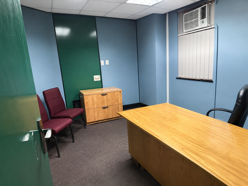 A functional office space featuring carpet flooring, a suspended ceiling, and a built-in window air conditioning unit.
