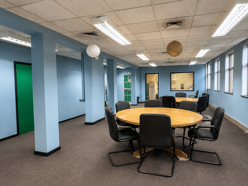 A functional commercial office space featuring suspended ceilings, fluorescent lighting, and carpeted flooring, suitable for a meeting room or collaborative workspace.