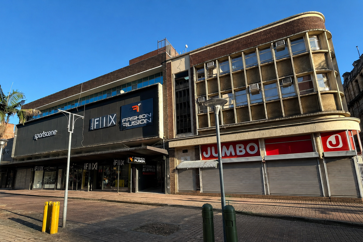 A commercial building facade featuring multiple retail storefronts with metal roller shutters, large display windows, and a prominent street-level entrance.