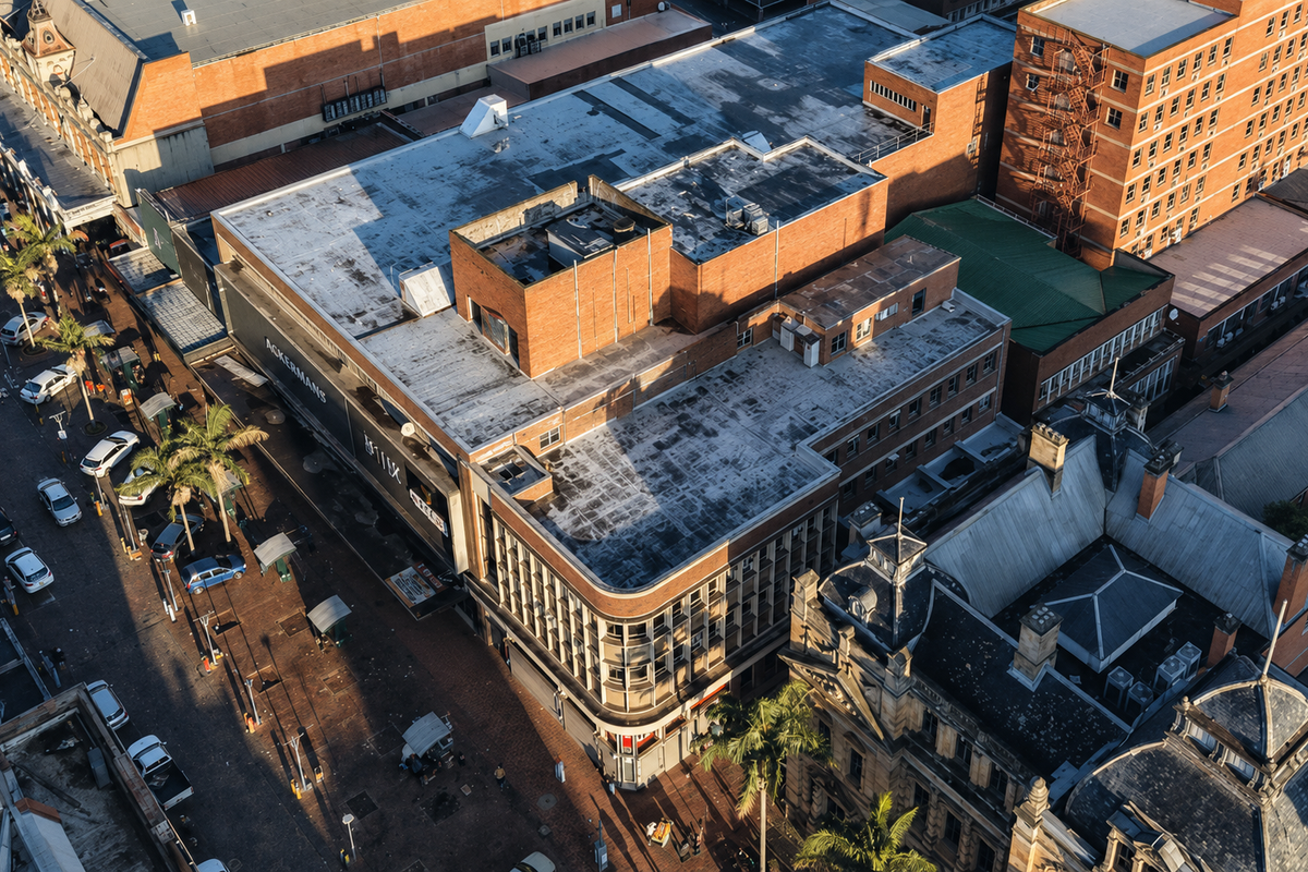 Aerial view of a commercial building complex featuring a flat roof, brick exterior, and street-level retail frontage in an urban setting.