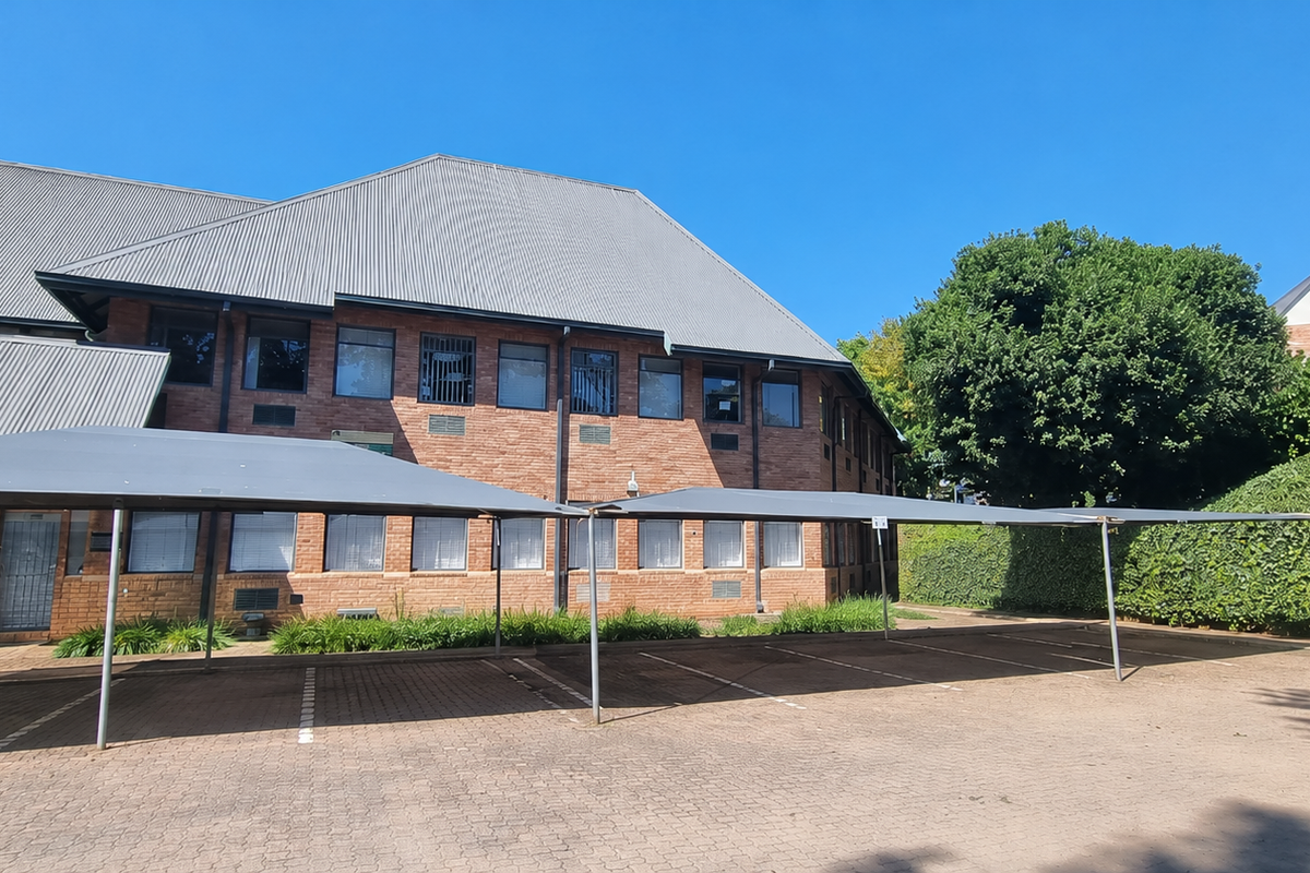 Rear view of a brick office building featuring a metal roof, paved parking area with shade cloth carports, and established perimeter landscaping.