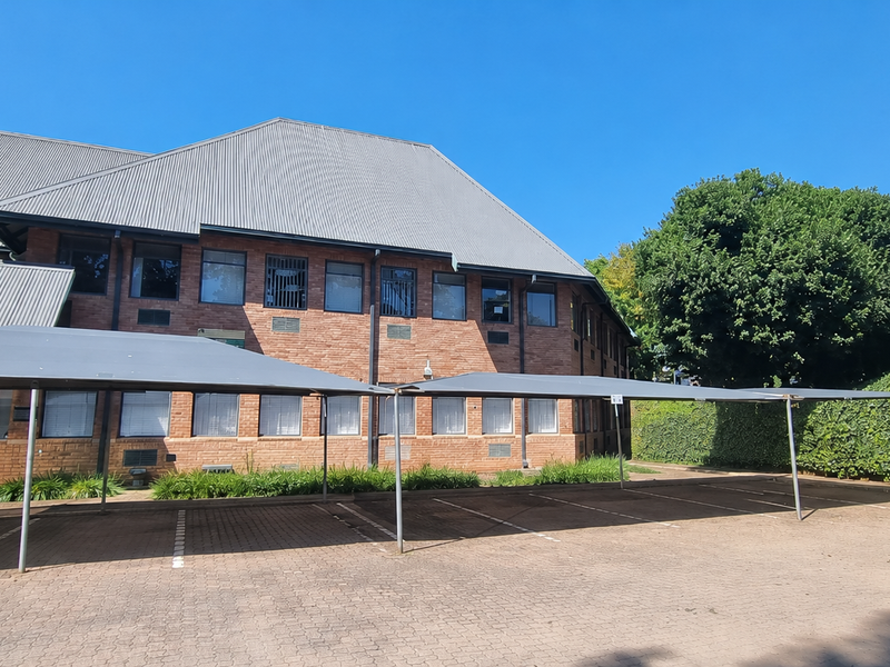 Rear view of a brick office building featuring a metal roof, paved parking area with shade cloth carports, and established perimeter landscaping.