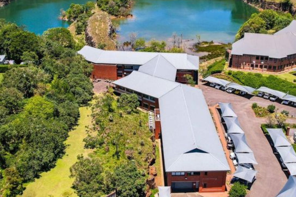 Aerial view of a professional office complex featuring multiple brick buildings with metal roofing, extensive landscaped grounds, and dedicated covered parking areas.