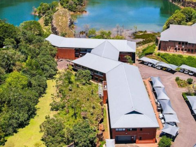 Aerial view of a professional office complex featuring multiple brick buildings with metal roofing, extensive landscaped grounds, and dedicated covered parking areas.