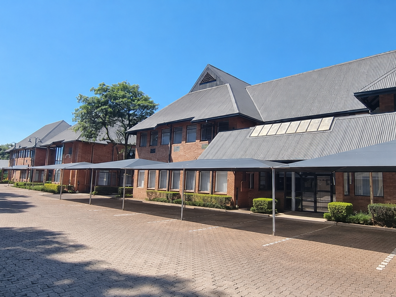 Exterior view of a professional office complex featuring a brick facade, pitched metal roofing, and extensive paved parking with shade cloth carports.