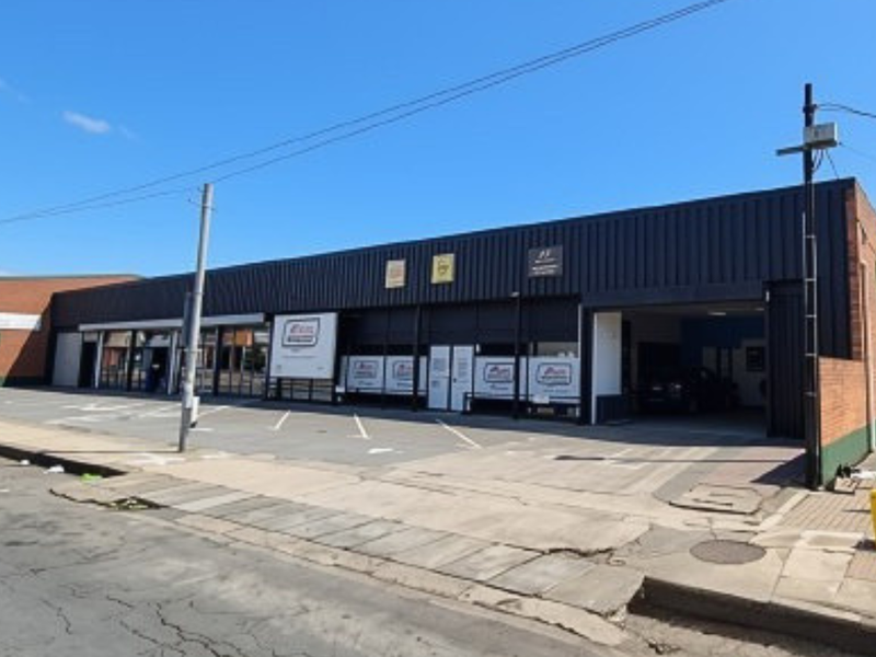 Front elevation of an industrial property featuring metal cladding, roller shutter access, and a paved driveway area.