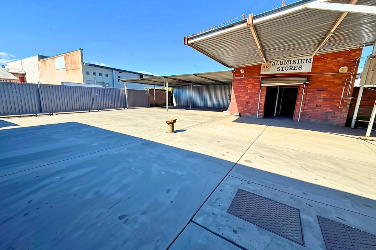 Spacious industrial concrete yard featuring a covered loading area, brick facade, and secure metal perimeter fencing.