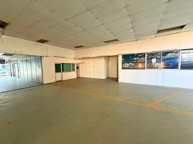 Spacious open-plan industrial unit featuring concrete flooring, suspended ceiling grid, and large glass windows, suitable for showroom or workshop use.