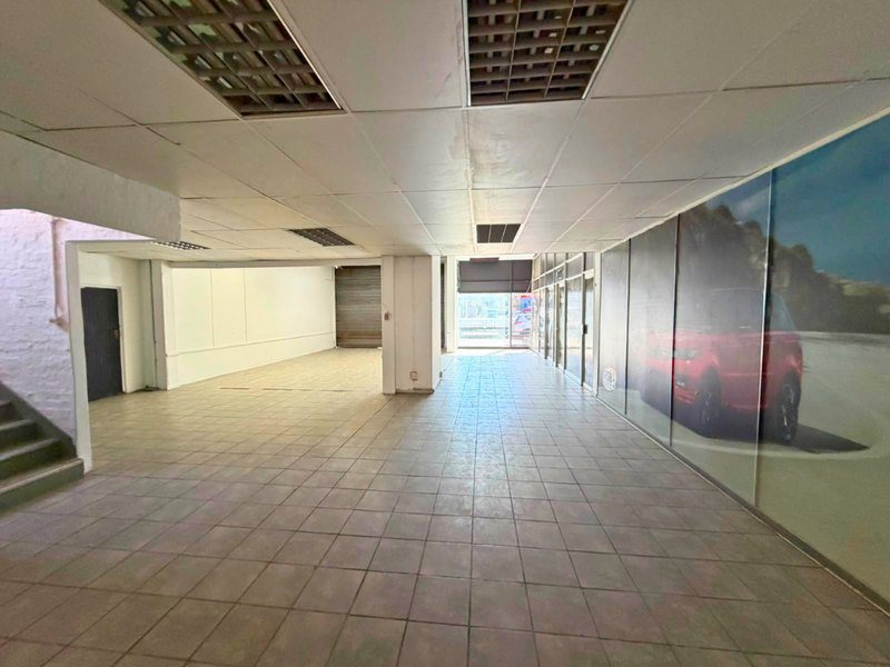 Spacious open-plan industrial showroom or retail space featuring tiled flooring, suspended ceilings, and a large glass storefront with a roller shutter door.