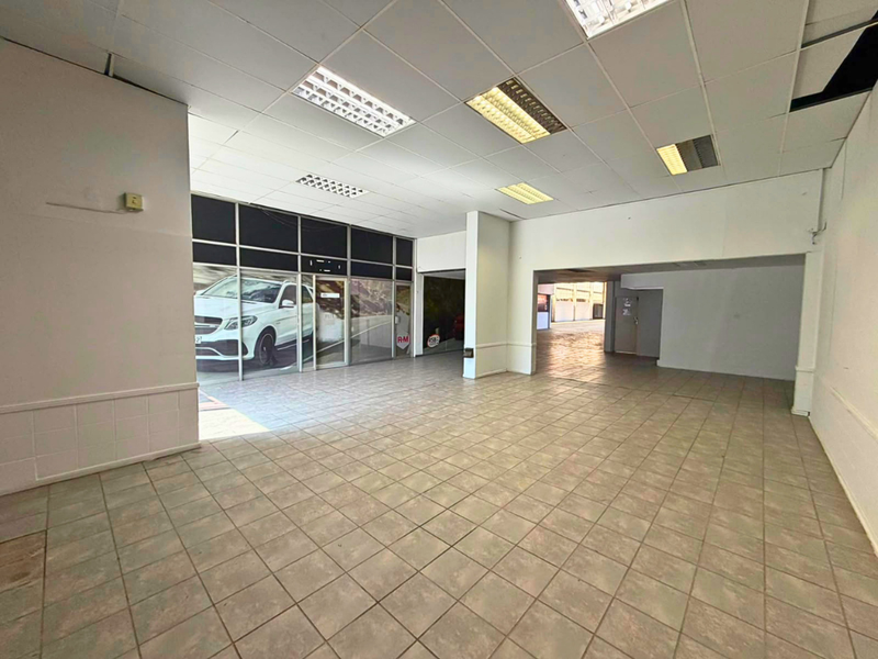 Spacious open-plan industrial or commercial unit featuring tiled flooring, suspended ceilings with recessed lighting, and a large glass storefront facade.
