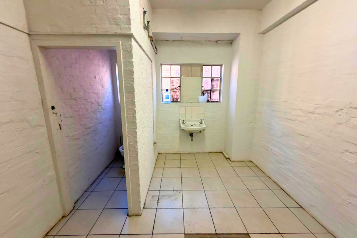 A basic, empty industrial-style bathroom featuring exposed brick walls, tiled flooring, and a wall-mounted basin.