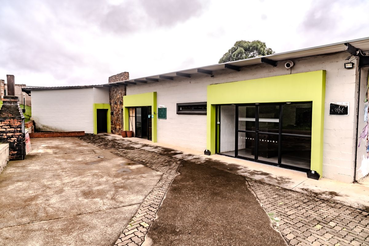 Exterior view of a commercial building featuring a paved courtyard, modern glass entrance doors, and lime green architectural accents.