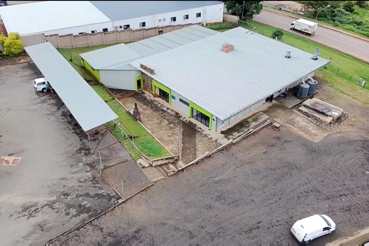 Aerial view of a commercial property featuring a metal roof structure, covered parking bays, and surrounding paved and unpaved yard space.