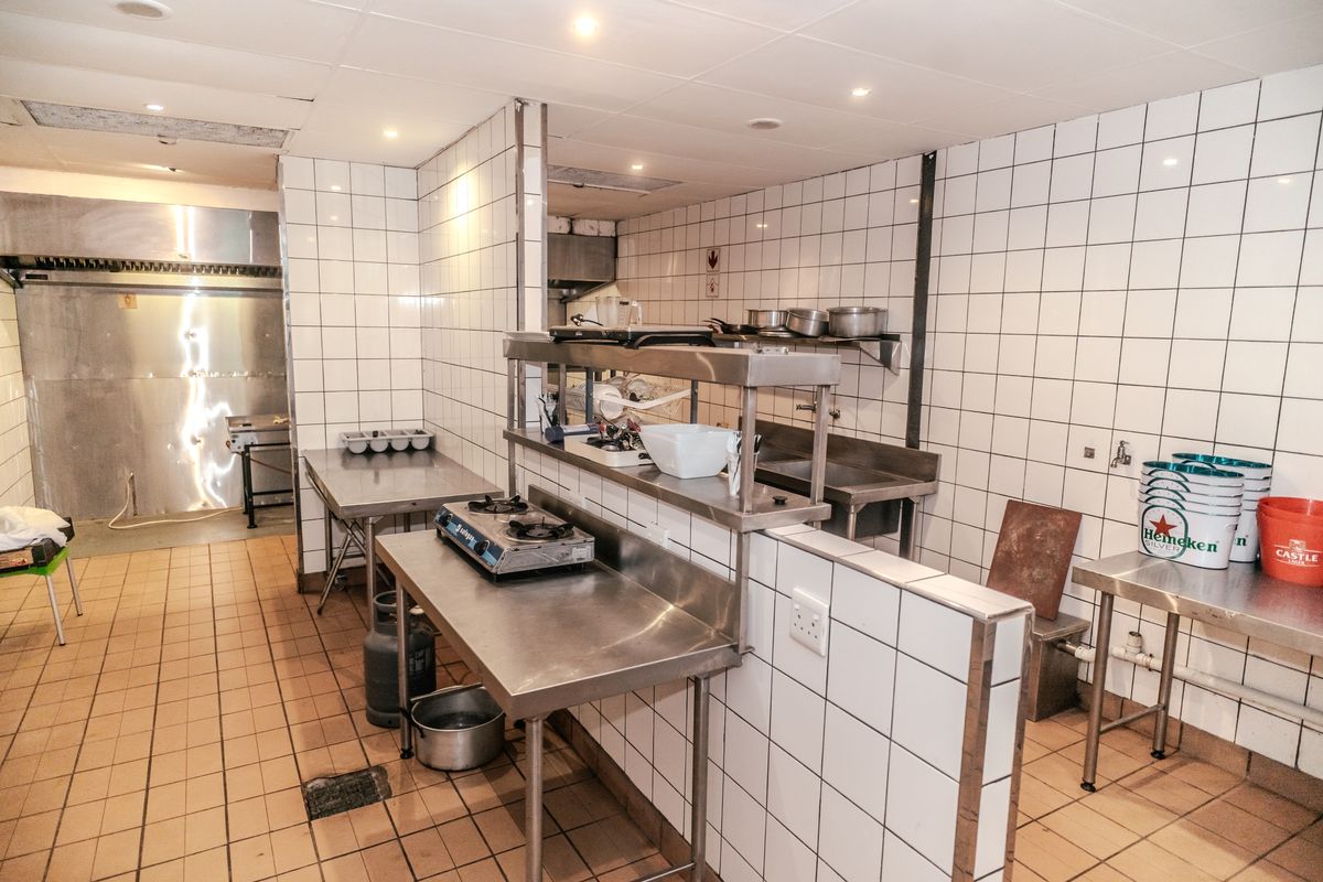 Commercial kitchen area featuring stainless steel prep tables, tiled walls, and integrated cooking stations, suitable for high-volume food preparation.