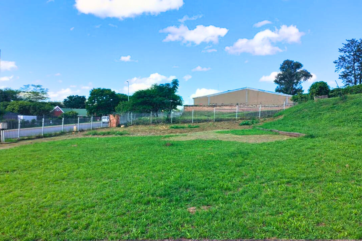 A view of the property grounds featuring a sloped grass lawn, perimeter fencing, and an industrial building in the background.