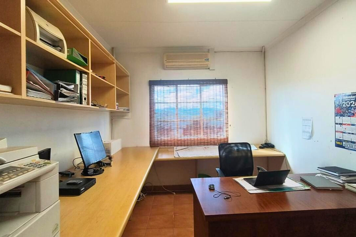 A functional office space featuring built-in wooden shelving, a long integrated desk, and a wall-mounted air conditioning unit.