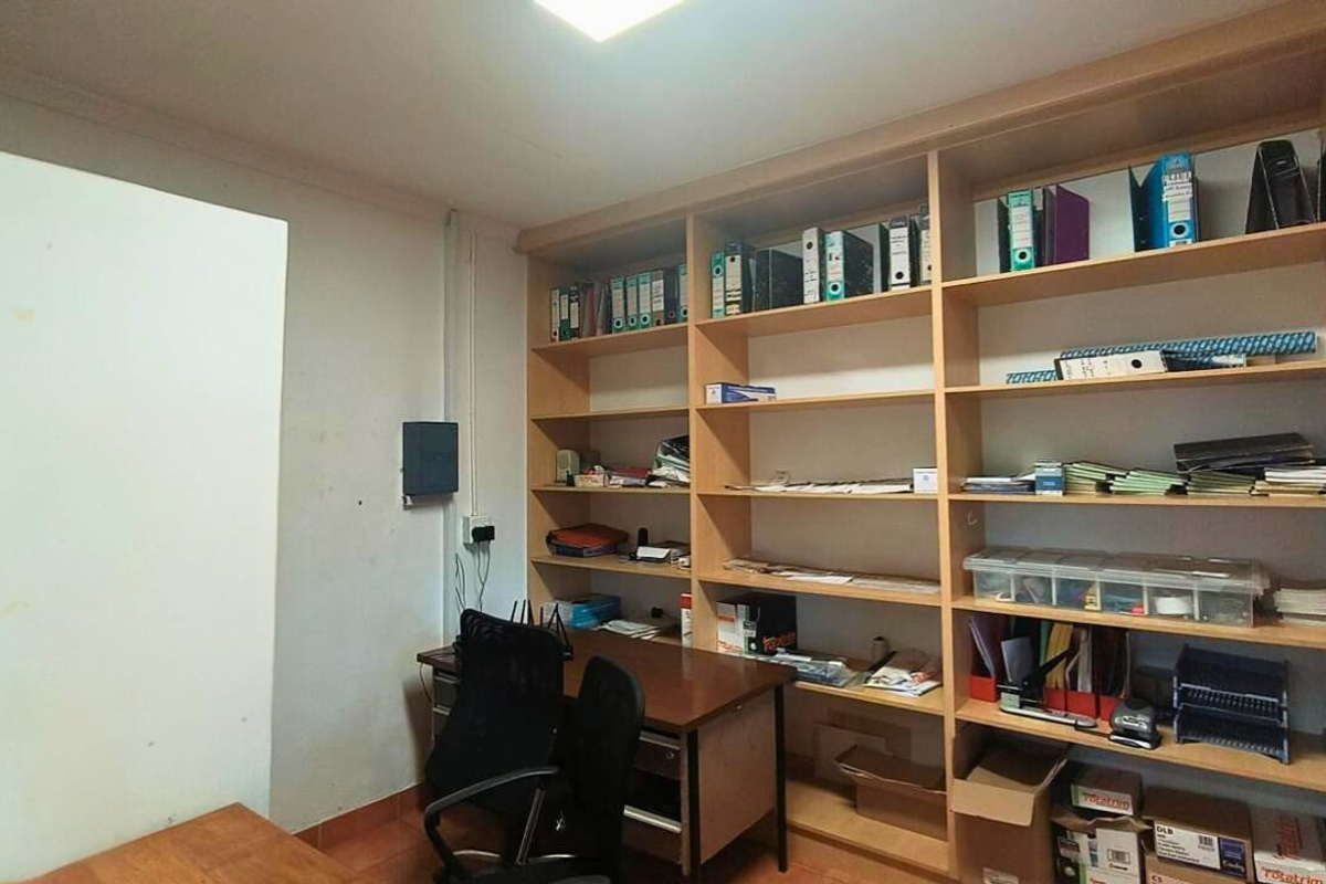 A functional office space featuring extensive built-in wooden shelving units, providing ample storage for documents and supplies in an industrial setting.