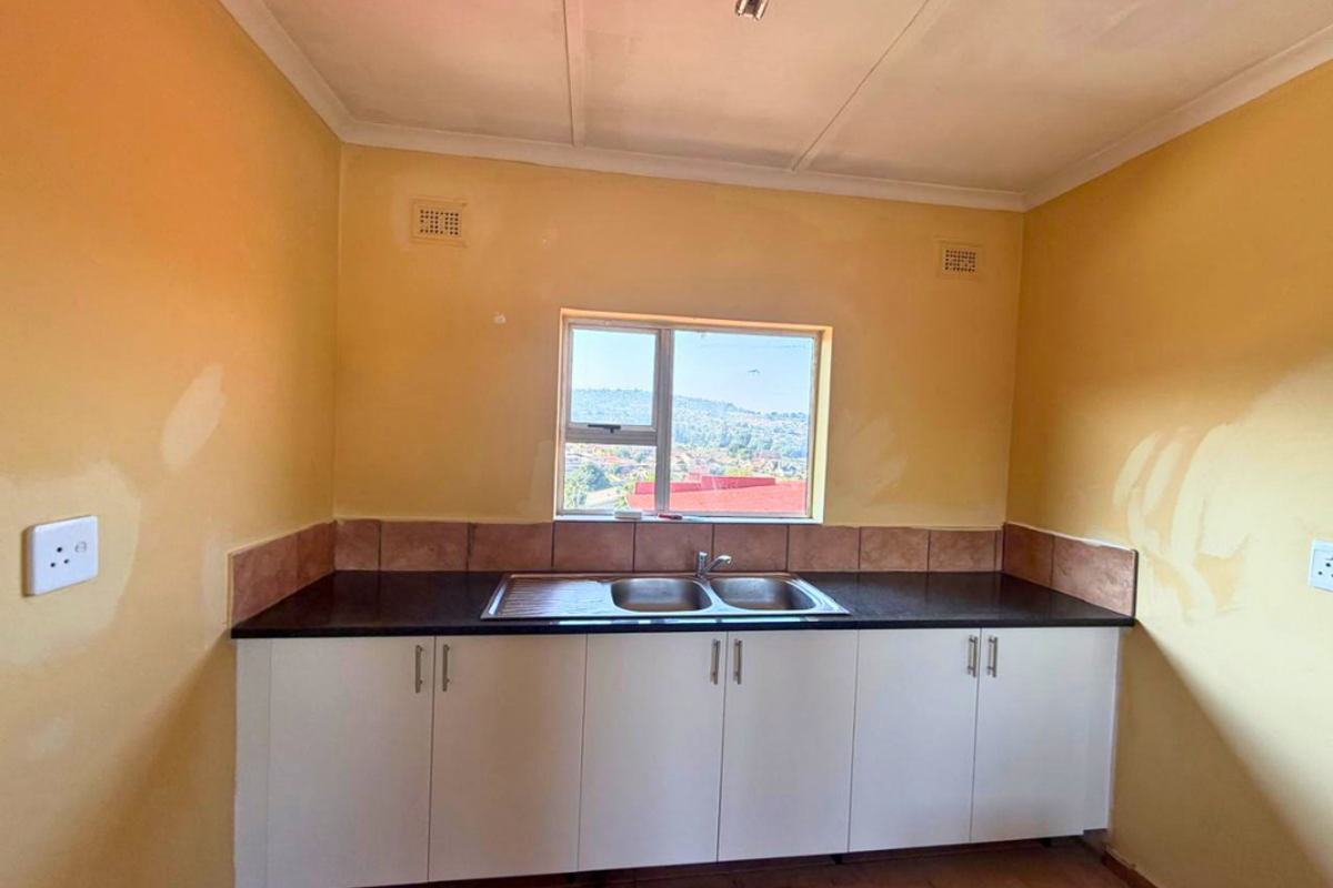 A compact kitchen area featuring white base cabinetry, a double bowl sink, and tiled backsplash, currently requiring wall finishing and painting.