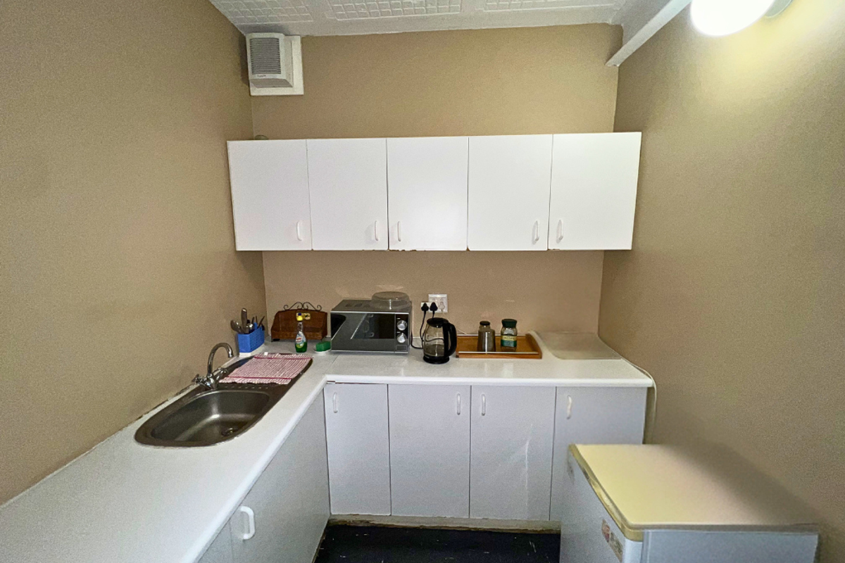 A compact kitchenette featuring white built-in cabinetry, a stainless steel sink, and a laminate countertop, suitable for a small office or utility space.