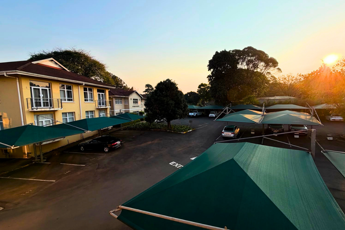 Exterior view of a commercial property featuring a paved parking lot with multiple shade cloth carports and multi-story building facades.