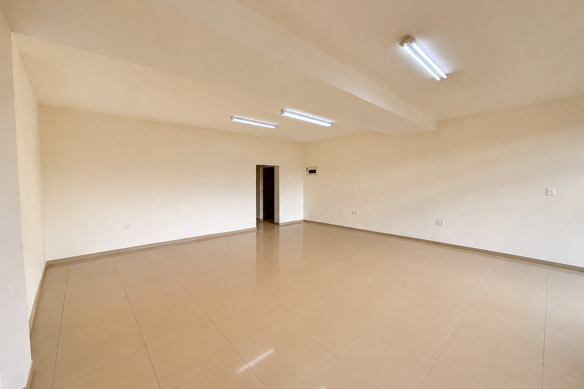 A spacious, empty open-plan area featuring neutral walls, ceramic tiled flooring, and functional overhead fluorescent lighting, suitable for various business or office configurations.