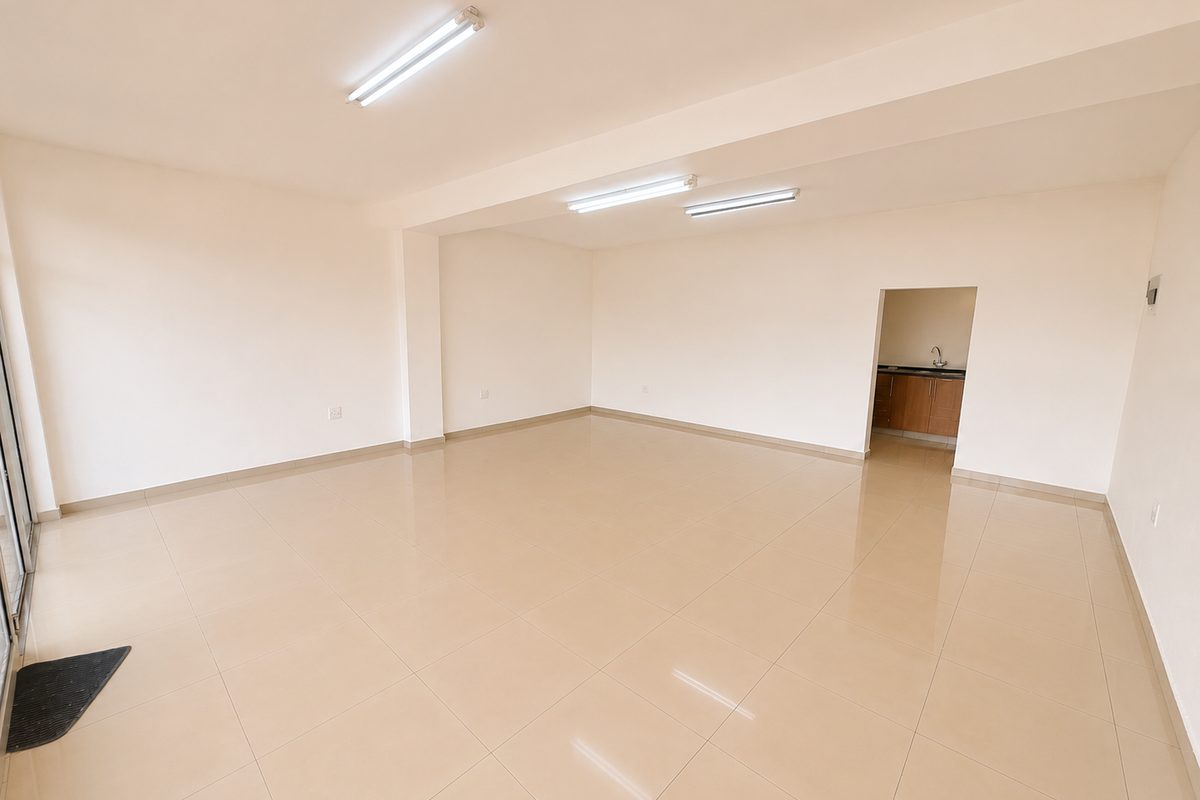 Spacious open-plan commercial area featuring neutral tiled flooring, bright overhead lighting, and a separate small kitchenette alcove.