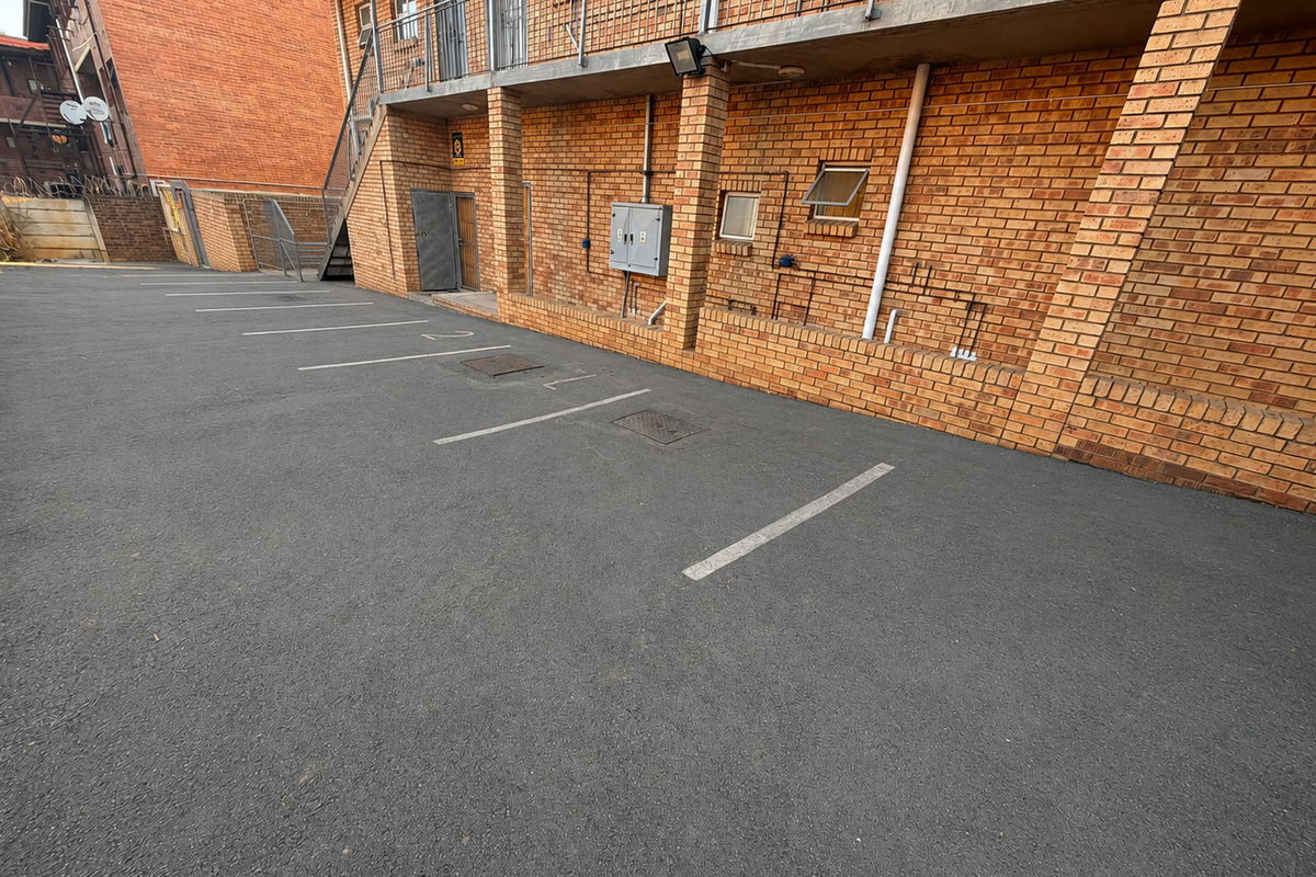 Rear exterior view of a commercial building featuring a paved parking area, brick facade, and external metal staircase access to the upper level.