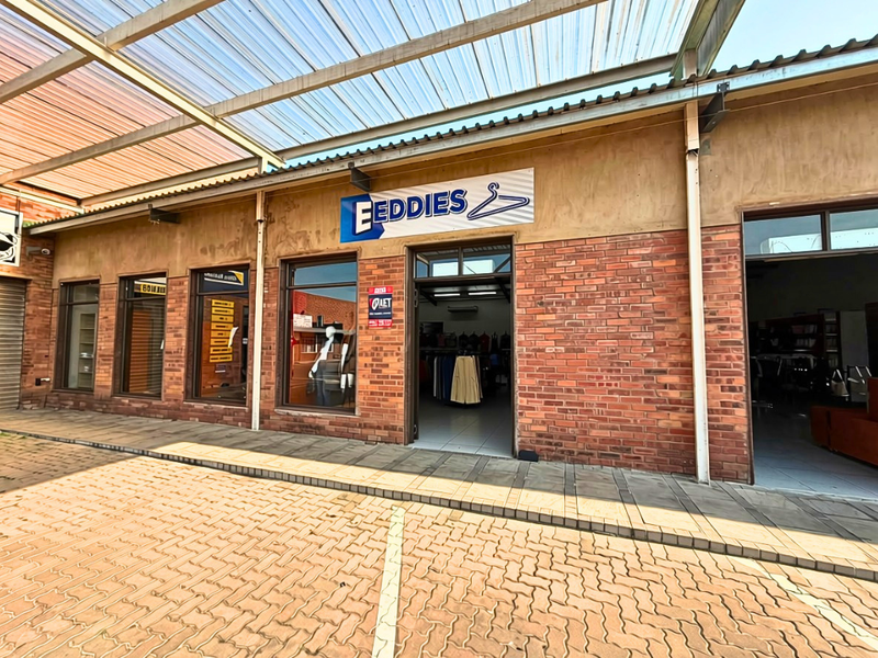 Commercial storefront featuring a brick facade, large display windows, and a covered walkway area with a translucent roof canopy.
