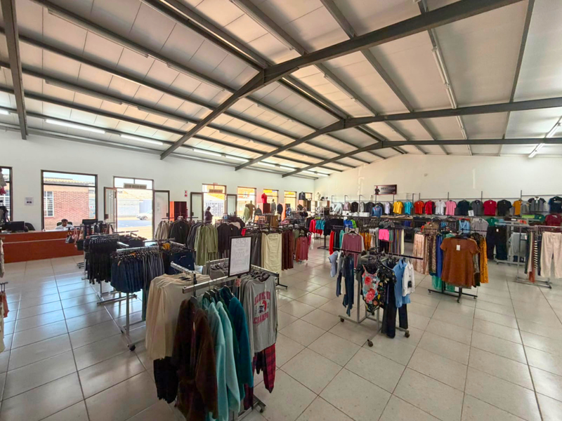 Spacious open-plan commercial retail space featuring high exposed steel roof trusses, tiled flooring, and ample natural light through large windows.
