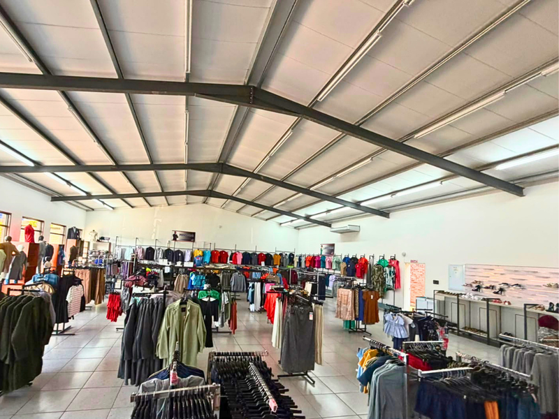Spacious commercial retail floor featuring high ceilings with exposed steel trusses, tiled flooring, and integrated lighting, suitable for various retail or showroom operations.
