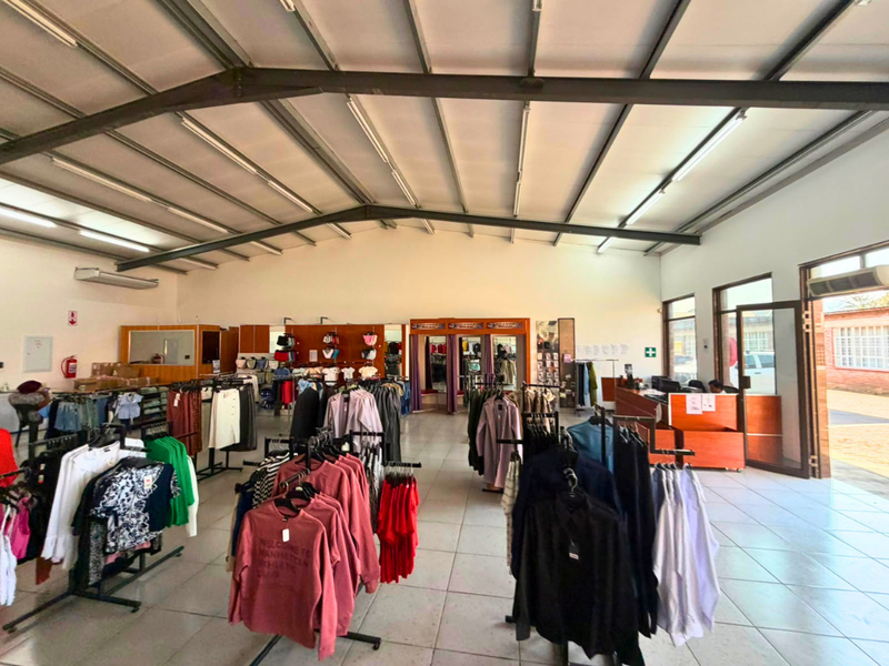Spacious open-plan commercial retail area featuring exposed steel roof trusses, tiled flooring, and integrated air conditioning, suitable for various business operations.