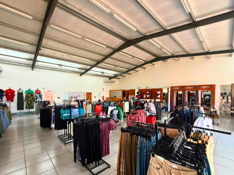 Spacious commercial retail floor featuring high exposed steel roof trusses, tiled flooring, and integrated fitting rooms with efficient overhead lighting.