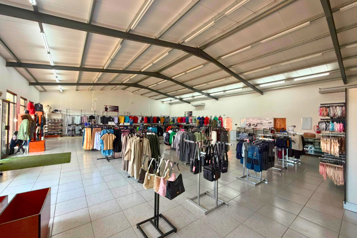 Spacious open-plan commercial retail space featuring high ceilings with exposed steel trusses, tiled flooring, and integrated lighting, suitable for various retail operations.