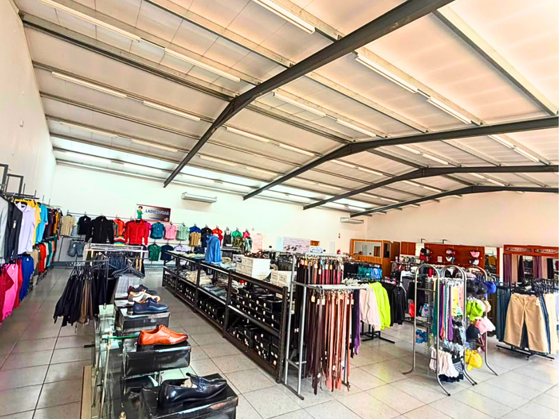 Spacious commercial retail area featuring high ceilings with exposed steel trusses, tiled flooring, and integrated lighting, suitable for various retail operations.