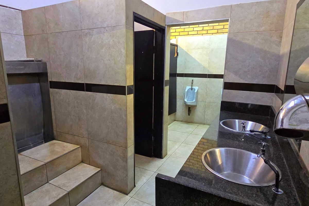 Commercial restroom facility featuring granite vanity with dual stainless steel sinks, tiled walls, and partitioned cubicles with wall-mounted urinals.