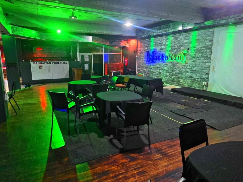 Spacious commercial clubhouse area featuring exposed brick walls, concrete ceilings, hardwood flooring, and a raised stage platform suitable for events.