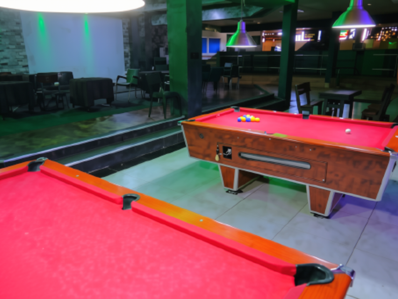 Spacious commercial sports facility featuring multiple pool tables, raised platform area, stone accent wall, and modern pendant lighting.